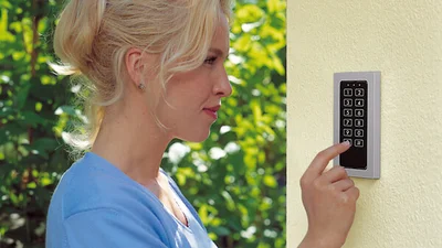 Das Bild zeigt eine Frau, die im Freien einen Zahlencode an einem Zutrittskontrollsystem mit Tastenfeld eingibt.