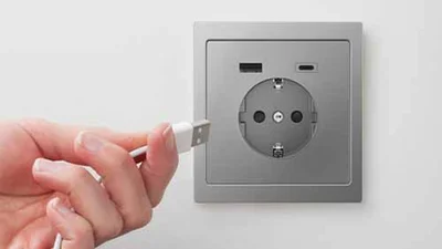 Person hält ein USB-Kabel in der Hand und will es in die silberne Steckdose mit USB stecken.