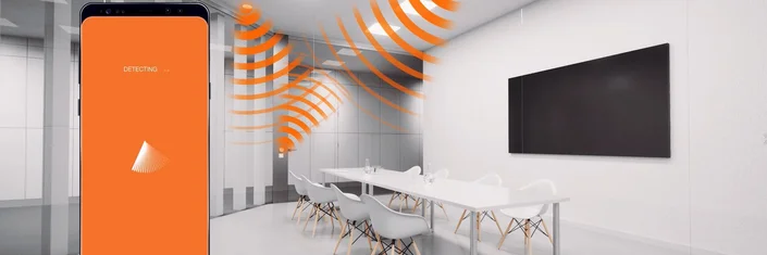 LEDVANCE HCL - Lichtsystem Das Bild zeigt einen Besprechungsraum, in dem grafisch Funkwellen zwischen Leuchten und einer Steuereinheit dargestellt sind. Im Vordergrund ist ein Handy mit zu sehen. Auf dem Display des Handys steht Detecting.