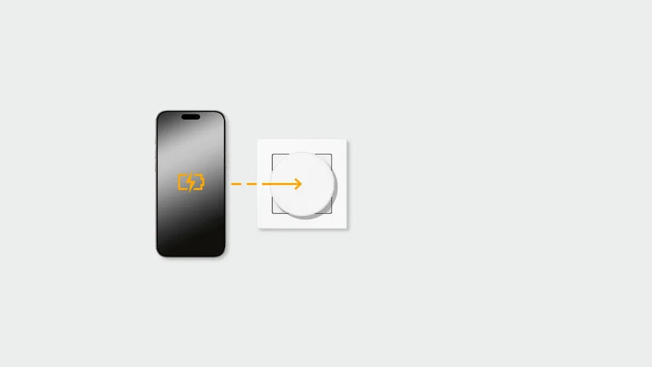 Das Bild zeigt ein Smartphone mit Batteriesymbol neben einem runden Wandschalter oder Ladepad. Ein Pfeil zwischen beiden deutet auf eine kabellose oder magnetische Energieübertragung bzw. Ladefunktion hin.