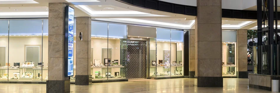 Ladenzeile in einem Einkaufszentrum mit Blick auf einen Juwelier außerhalb der Öffnungszeiten und mit Ladenschutzgitter.