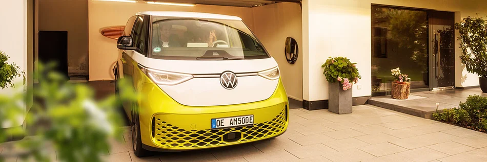 Das Bild zeigt ein Elektroauto der Marke Volkswagen in einer Garagenauffahrt. An der Wand der Garage ist eine Wallbox montiert. Vor dem Haus stehen Pflanzen in Töpfen.