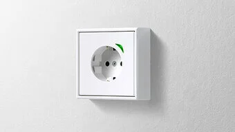 Das Bild zeigt eine weiße Steckdose des Herstellers Jung, die an einer grauen Wand installiert wurde