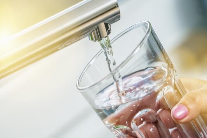 Glas in das Wasser fliesst. Glas wird von einer Hand gehalten.