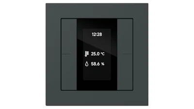 Ein schwarzer Gira Tastsensor mit integriertem Display ist auf weißem Hintergrund zu sehen. Das Display zeigt Uhrzeit, Temperatur und Luftfeuchtigkeit an.
