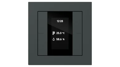 Ein schwarzer Gira Tastsensor mit integriertem Display ist auf weißem Hintergrund zu sehen. Das Display zeigt Uhrzeit, Temperatur und Luftfeuchtigkeit an.