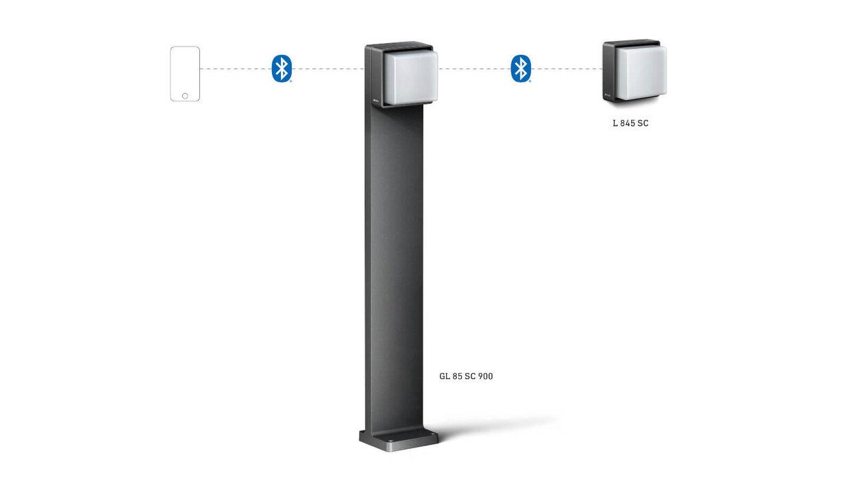 Das Bild zeigt eine vernetzte Außenleuchte der Steinel Cube Serie PRO mit Bluetooth. Die Abbildung zeigt die Verbindung zu weiteren Modulen und eine hohe, schlanke Lichtstele.