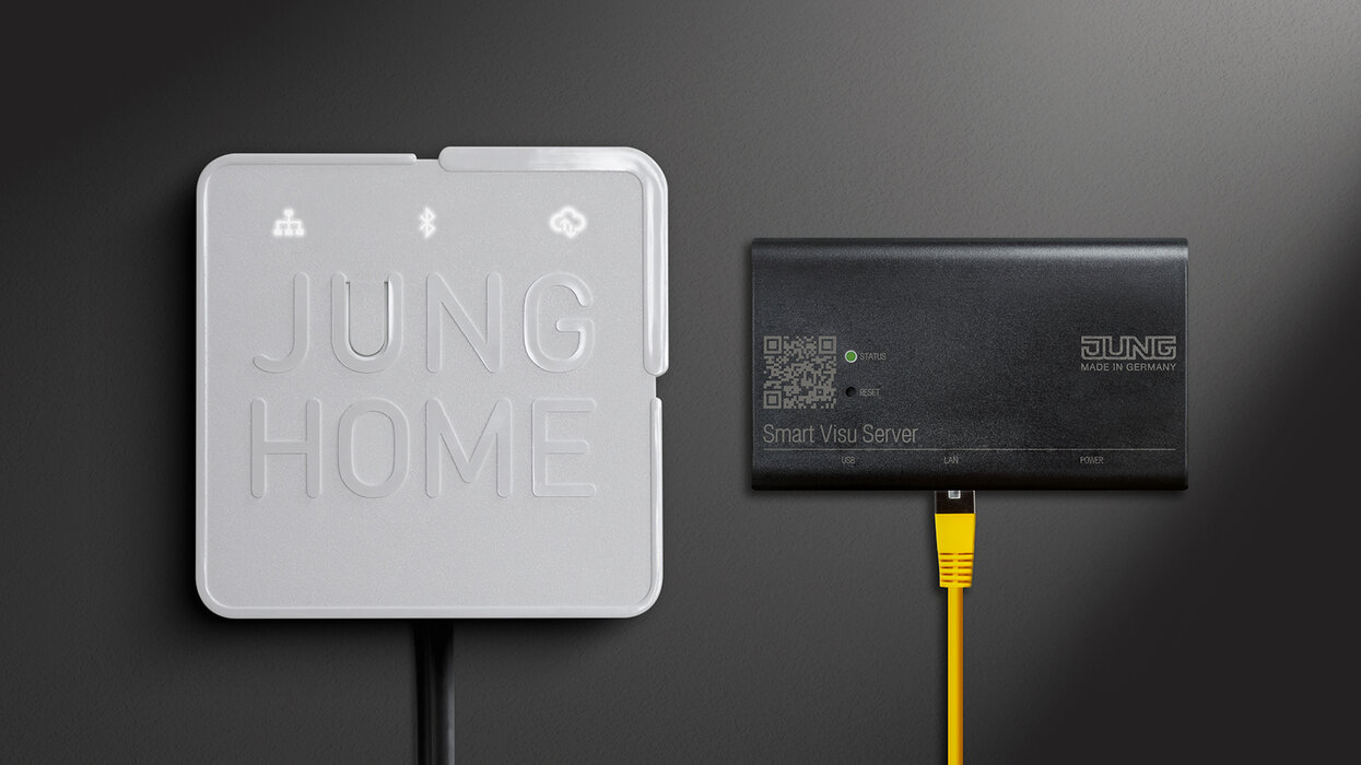 Smart HOME Bundle: JUNG HOME Gateway meets Smart Visu Server Nahaufnahme von zwei Geräten an einer Wand: das JUNG HOME Gateway (weiß) und der Smart Visu Server (schwarz) mit angeschlossenem gelbem Netzwerkkabel.
