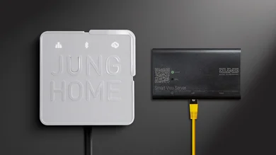 Nahaufnahme von zwei Geräten an einer Wand: das JUNG HOME Gateway (weiß) und der Smart Visu Server (schwarz) mit angeschlossenem gelbem Netzwerkkabel.