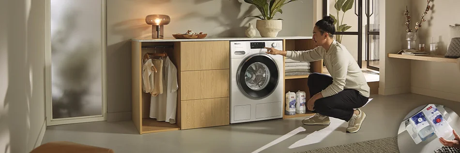 Eine Person bedient knieend eine Waschmaschine in einem hellen und modernen Hauswirtschaftsraum