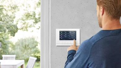 Das Bild zeigt Rückansicht einer Person in einem blauen Pullover, die ein Panel an einer weißen Wand bedient. 