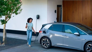 Eine Person schließt ein Elektroauto an eine Wallbox vor einem Wohnhaus zum Laden an.