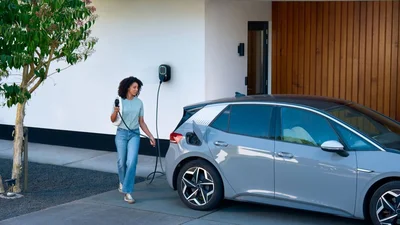 Eine Person schließt ein Elektroauto an eine Wallbox vor einem Wohnhaus zum Laden an.