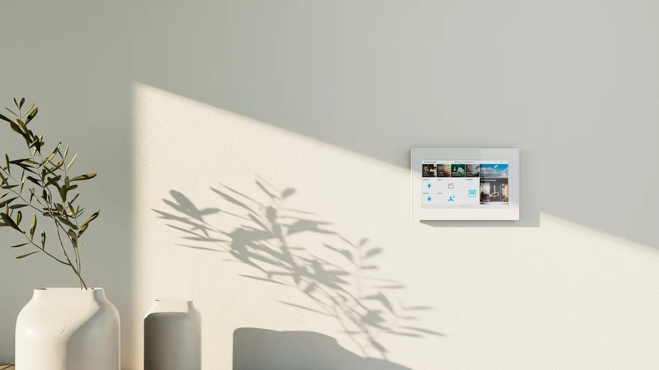 Das Bild zeigt einen weißen Busch-OneTouch 7" an einer hellen Wand. Daneben steht ein Sideboard aus hellem Holz, auf dem zwei weiße Vasen stehen. In einer Vase steckt ein Zweig. 