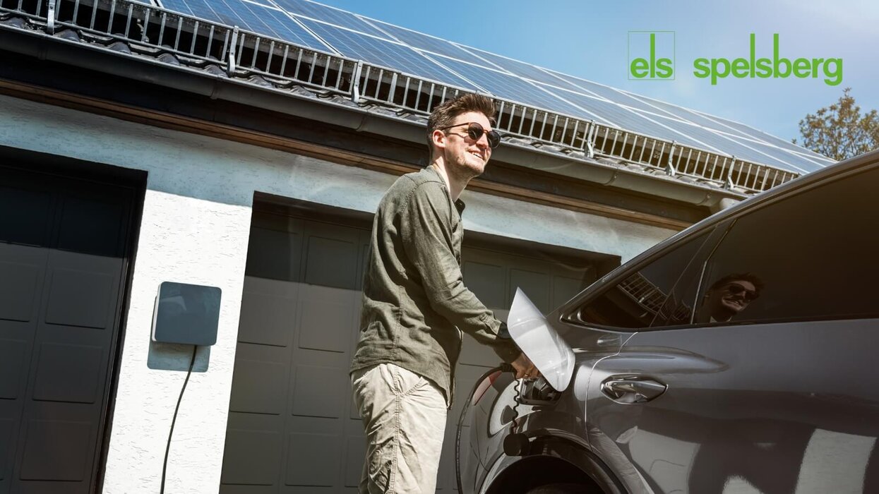 Ein Mann lädt ein Elektroauto an einer Hauswand mit montierter Wallbox. Auf dem Dach des Hauses sind Solarmodule installiert. Oben rechts befindet sich das Spelsberg-Logo.