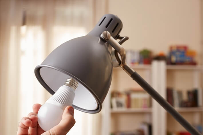 Person dreht eine LED-Birne in eine schwarze Stehlampe.
